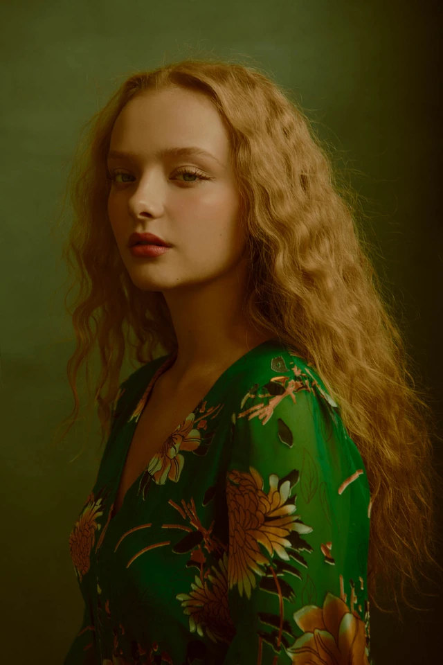 Actress Amiah Miller, star of War for the Planet of the Apes, in a green floral dress, long auburn waves, warm studio light.