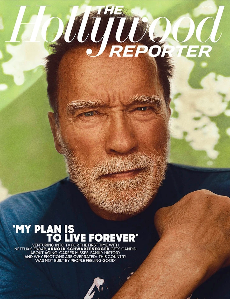 Actor Arnold Schwarzenegger of Netflix's FUBAR, intense gaze in a blue tee against soft green botanicals, for The Hollywood.