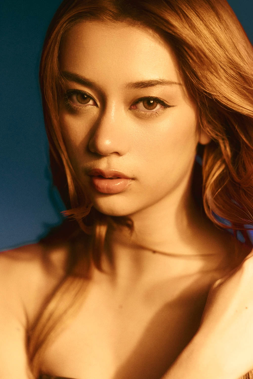 Megan of Grammy-nominated girl group Katseye, close portrait, warm amber light against cool blue, sharp liner and auburn.