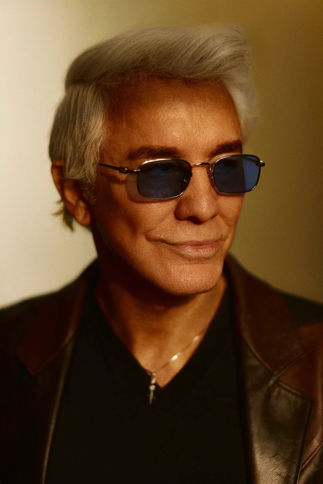 Director Baz Luhrmann, silver-haired in blue-tinted shades and a leather jacket, warm amber light catching a quiet smile.