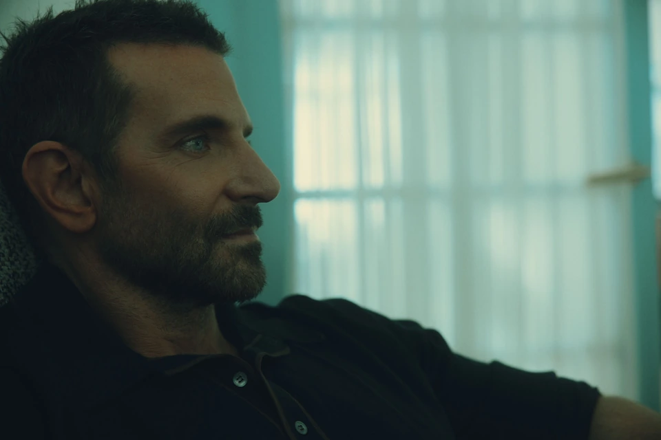 Actor and director Bradley Cooper in dark profile against teal-lit curtains, steady gaze off-frame, for The Hollywood.