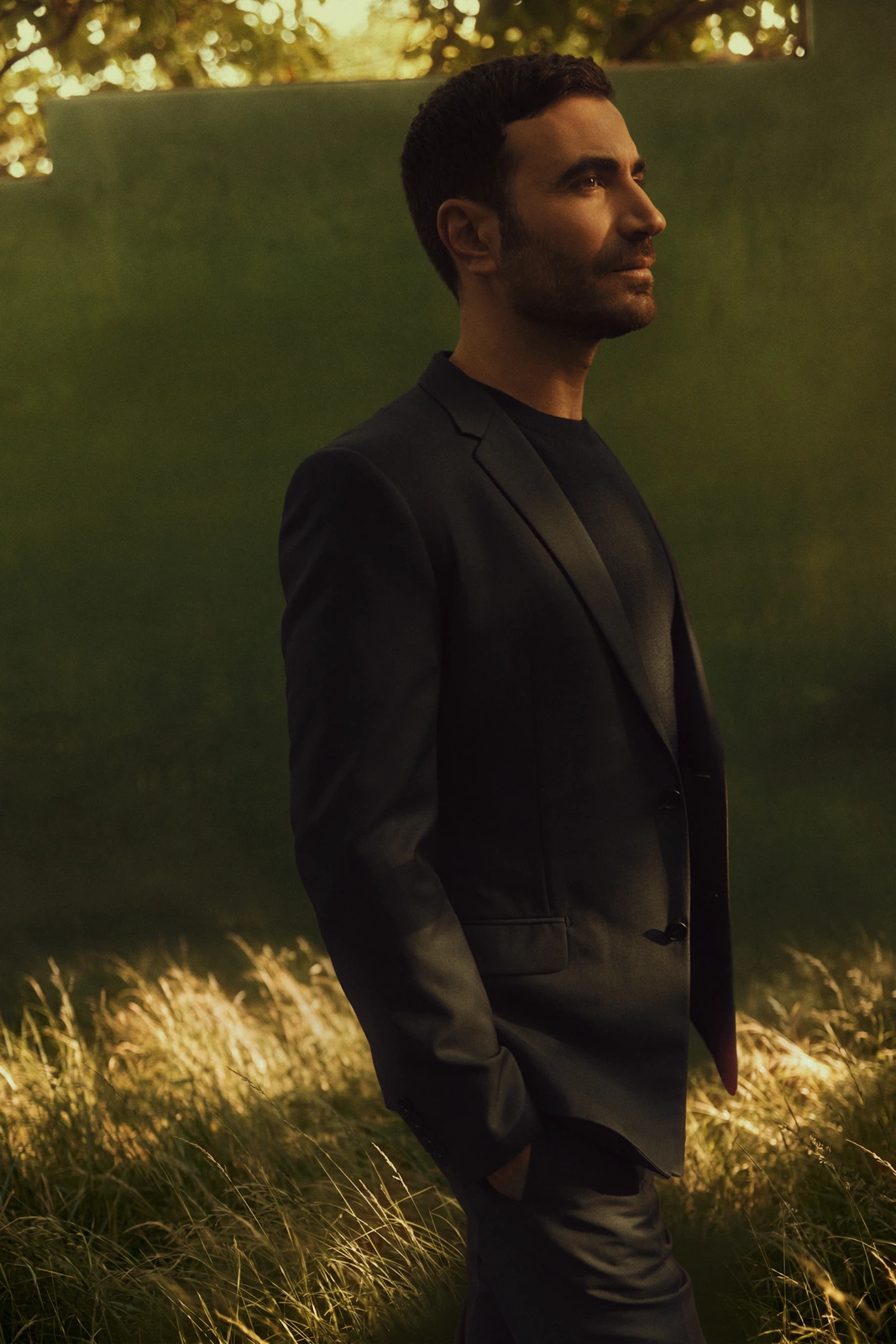 Actor Brett Goldstein, Emmy-winning star of Ted Lasso, in a dark blazer gazing off in golden-hour light against a lush green.