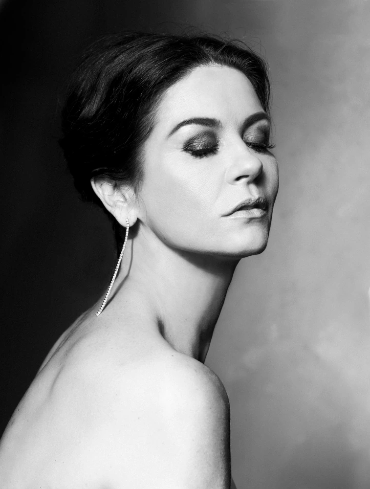 Actress Catherine Zeta-Jones, eyes closed, bare shoulder turned in B&W, long drop earring catching light against soft studio.