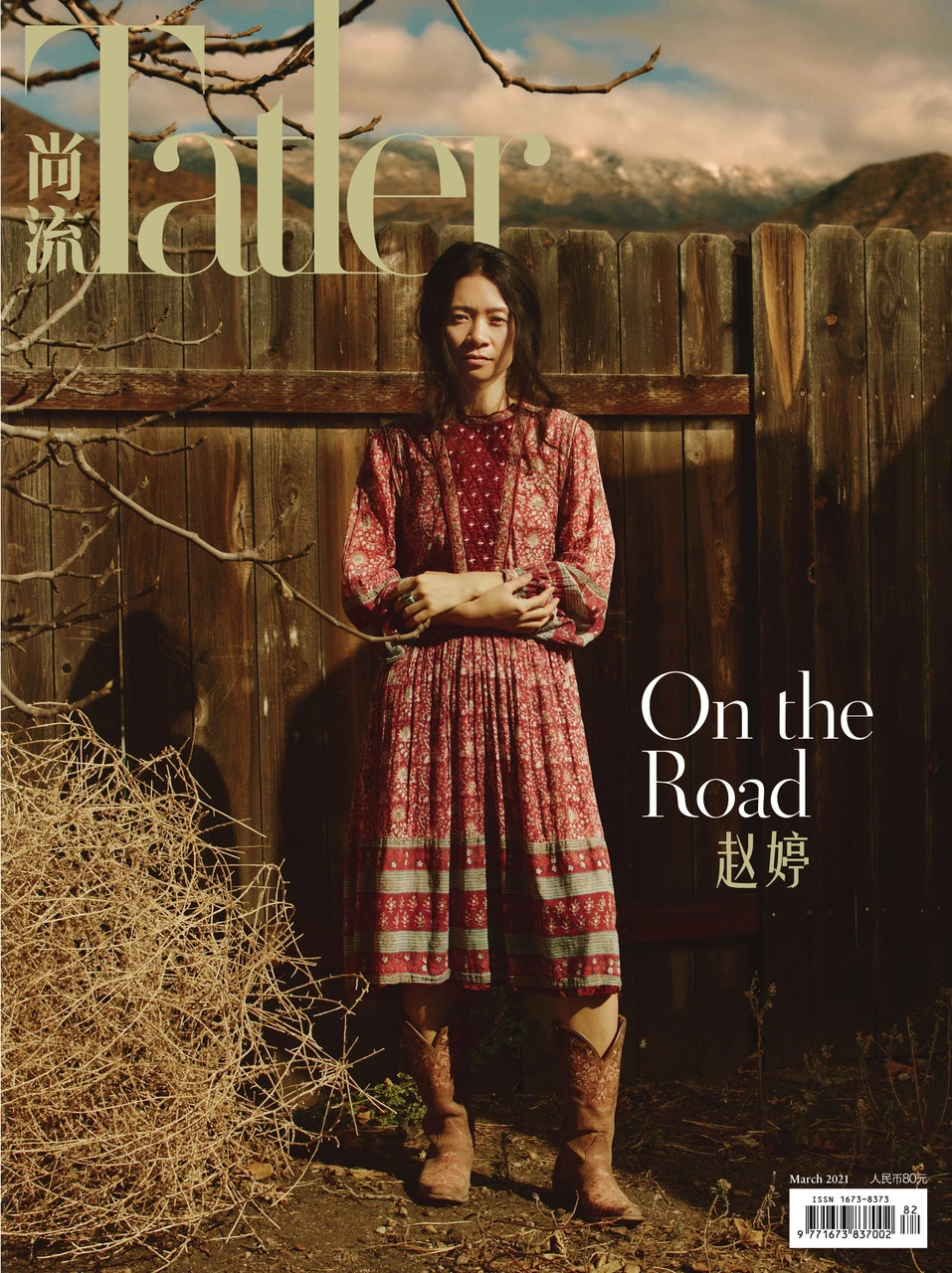 Director Chloé Zhao, Nomadland's Oscar winner, in a red floral prairie dress and cowboy boots against mountain landscape
