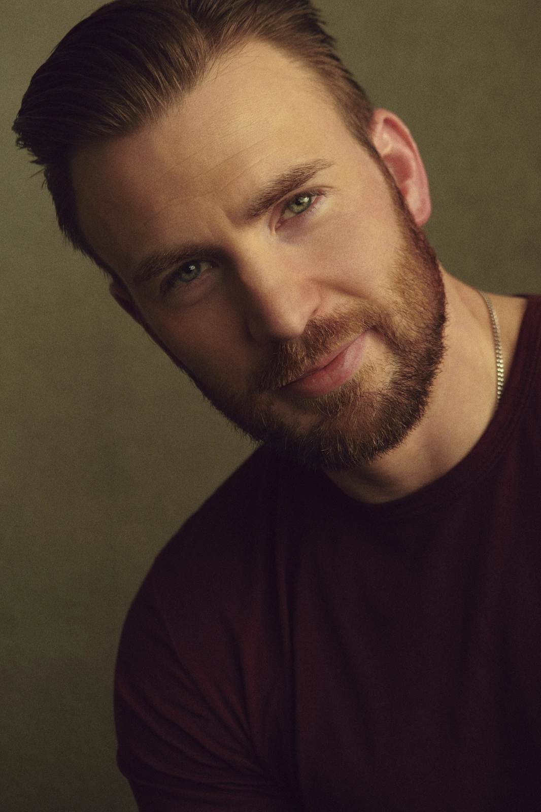 Actor Chris Evans, warm olive studio light catching green eyes, dark burgundy tee and silver chain, slight smile, by Austin.