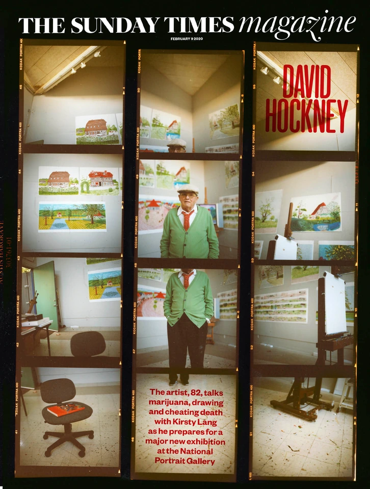 Artist David Hockney in a green cardigan and red tie amid his paintings, shot on film for The Sunday Times Magazine cover.
