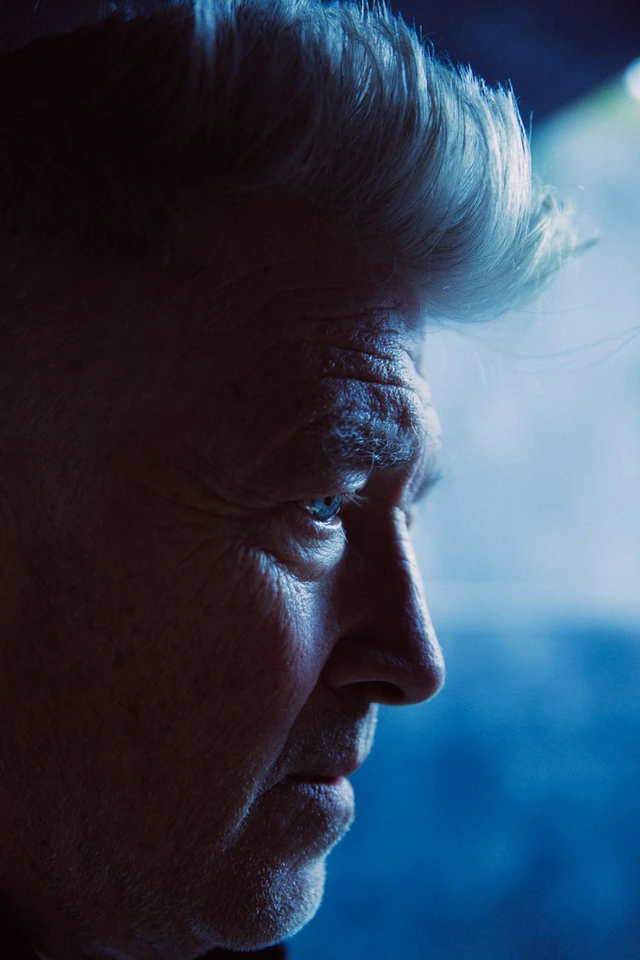 Director David Lynch in stark blue shadow, silver hair swept back, pale eyes distant in a tight profile portrait by Austin.