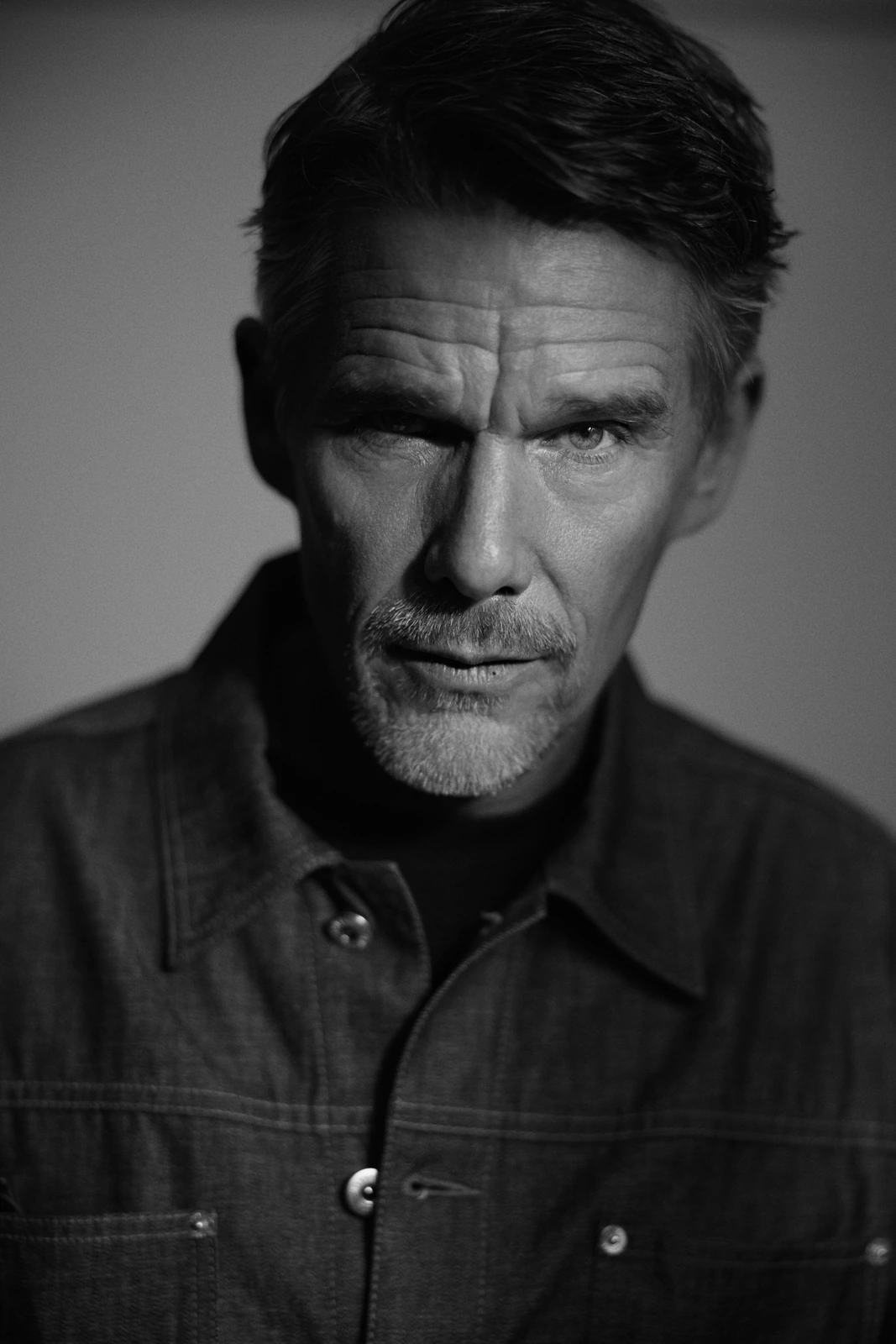 Actor and writer Ethan Hawke, intense gaze in close black-and-white portrait, goatee, denim jacket, deep shadow by Austin.