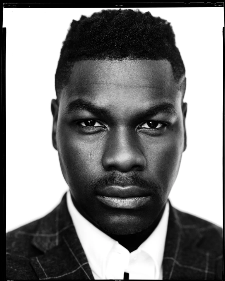 Actor John Boyega, unflinching gaze in a B&W large-format portrait, plaid blazer over white shirt, shot on film by Austin.