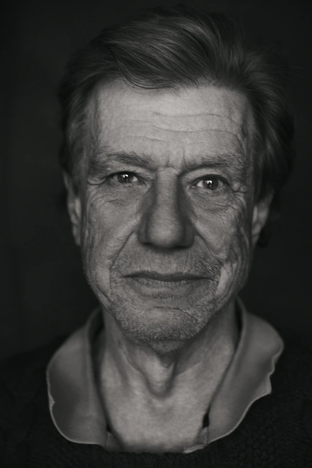 Director John McTiernan of Die Hard, intense gaze direct to camera in a stark black-and-white close portrait against deep.