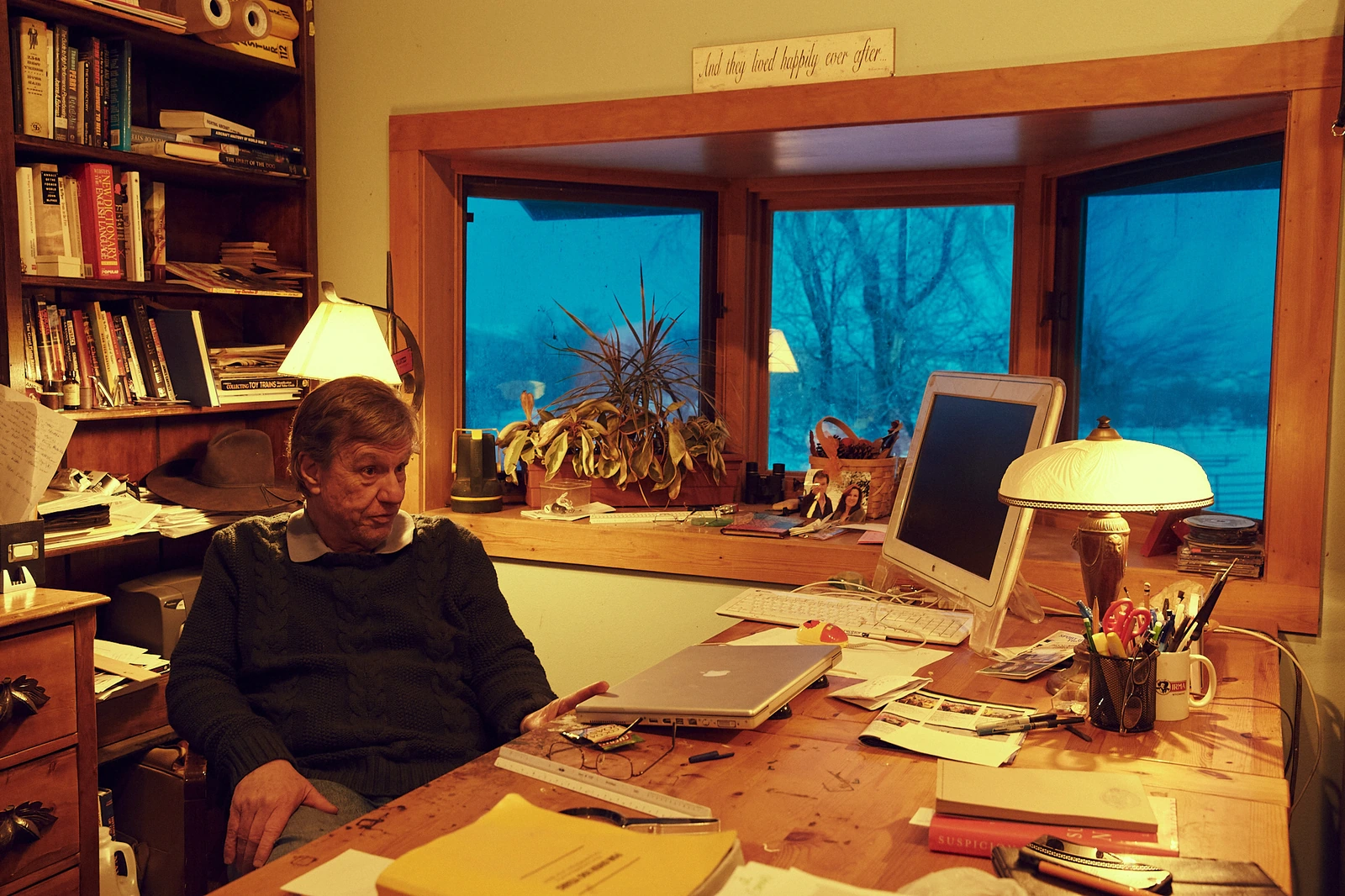 Director John McTiernan at a cluttered home desk, warm lamp glow against a deep blue winter window, dark sweater, thoughtful.