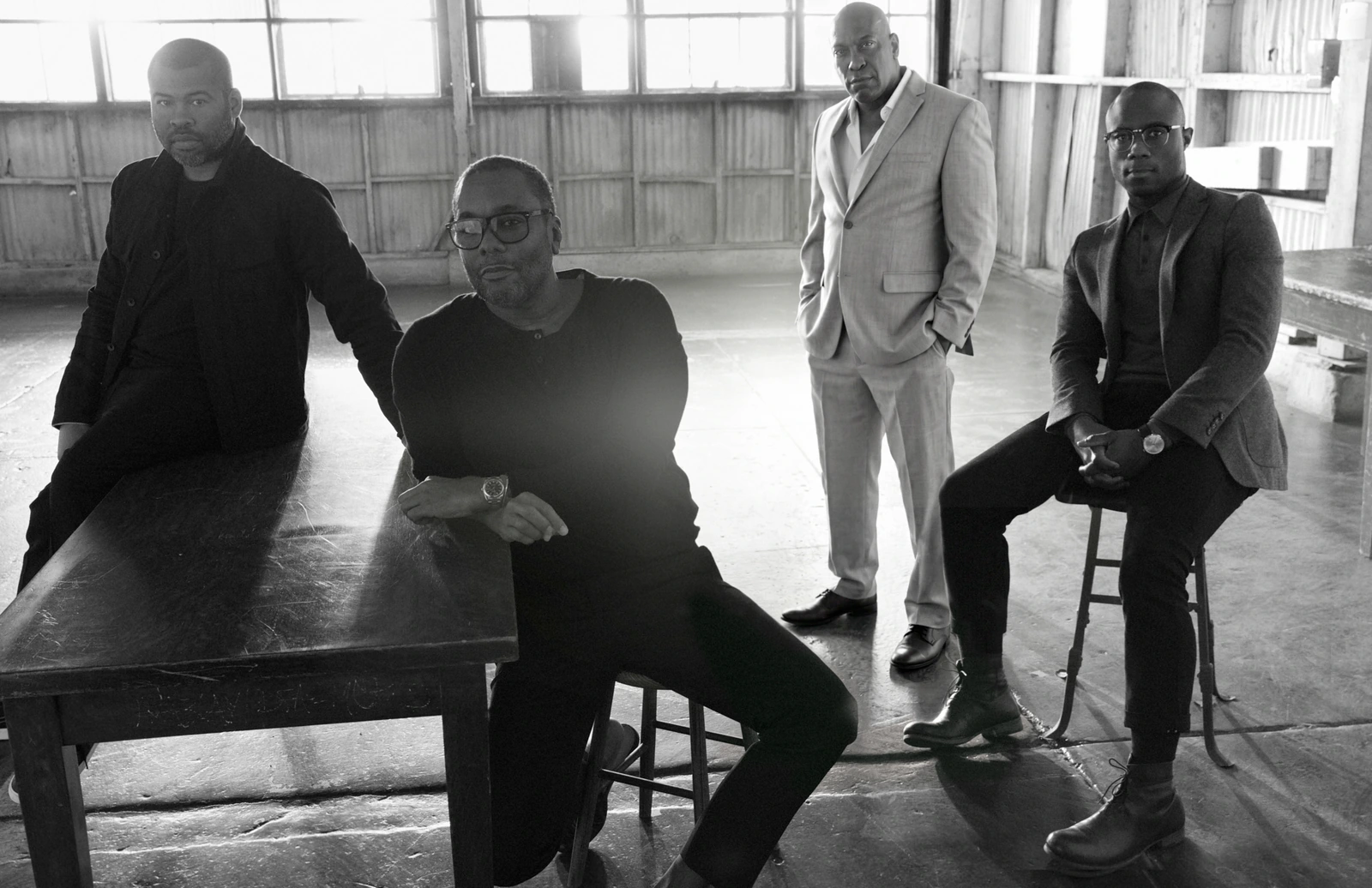Iconic Black Directors Jordan Peele, Steve McQueen, John Singleton, and Barry Jenkins in black and white, empty warehouse.