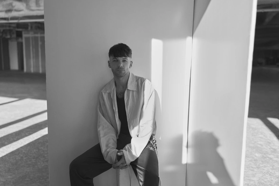Singer-songwriter Louis Tomlinson of , leaning against a white panel in sharp daylight shadow. by Austin Hargrave