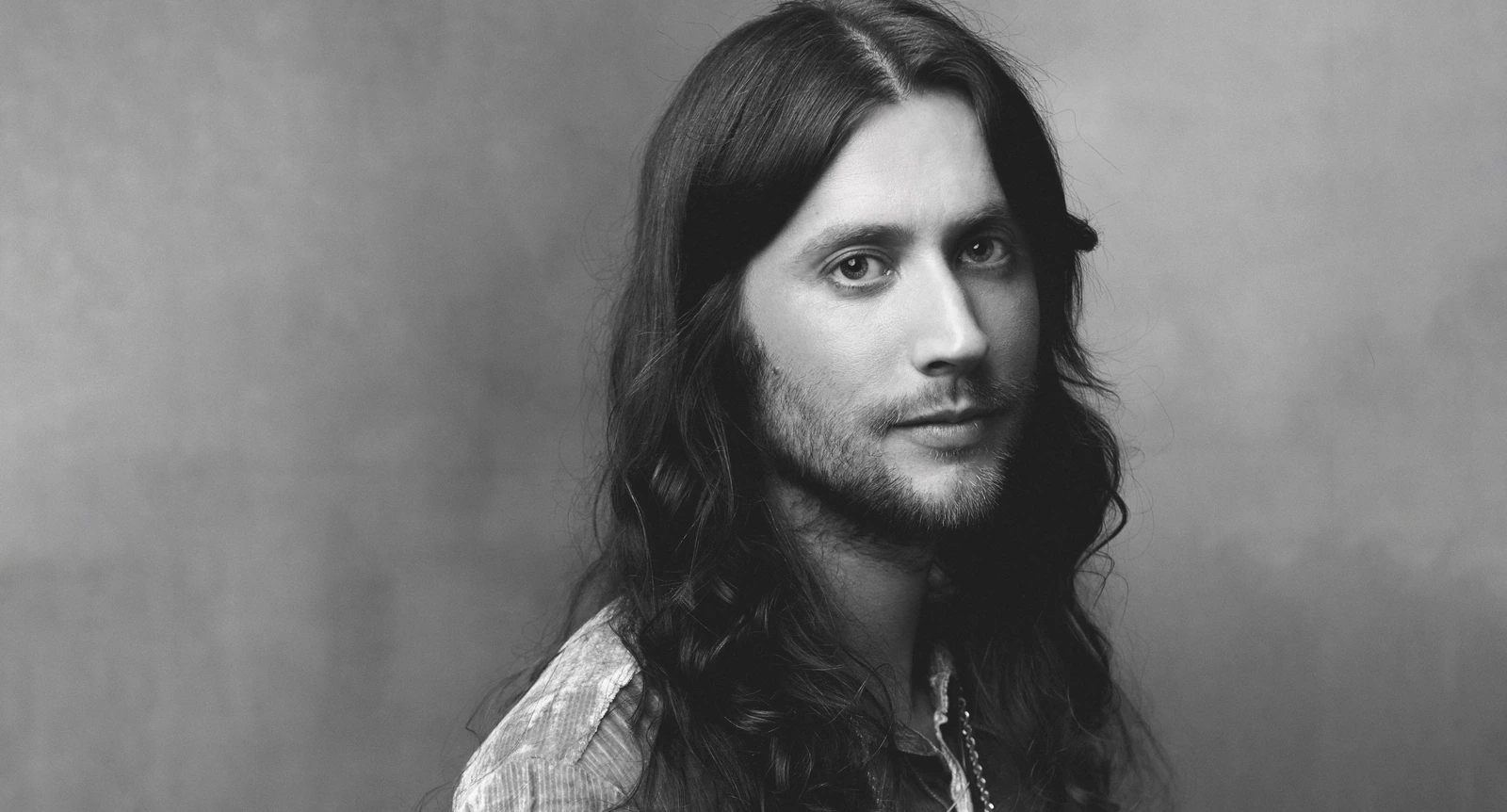Composer Ludwig Göransson, three-time Oscar winner, in B&W — long dark hair, open plaid shirt, quiet intensity against soft.