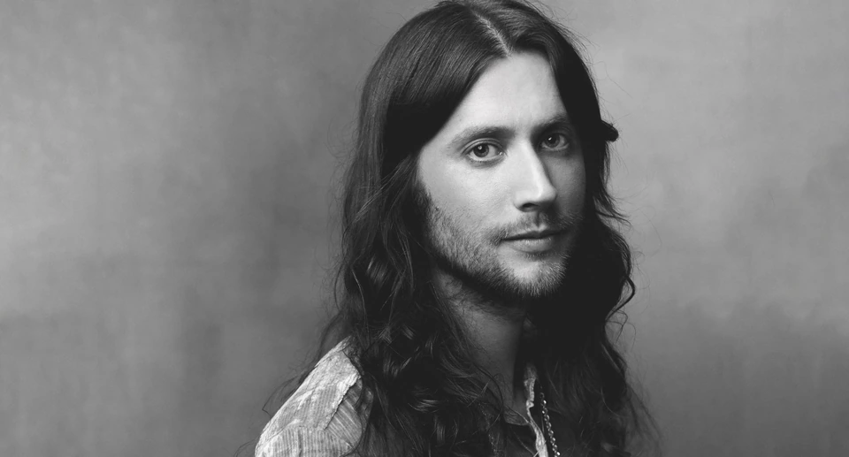 Composer Ludwig Göransson, three-time Oscar winner, in B&W — long dark hair, open plaid shirt, quiet intensity against soft.