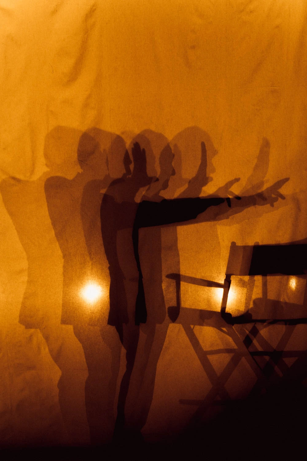 Director Martin Scorsese's silhouette cast in amber against draped canvas, arm outstretched mid-direction beside a film.