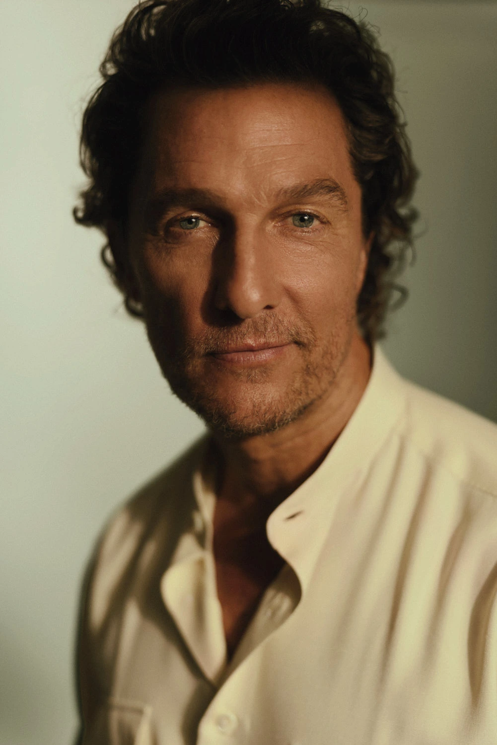 Actor Matthew McConaughey, warm amber light sculpting his face, open cream shirt, curly dark hair, quiet gaze. Photo Austin