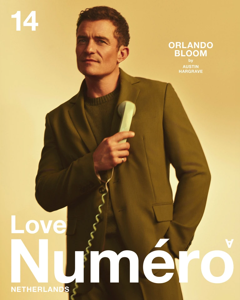 Actor Orlando Bloom in an olive suit holding a mint telephone, warm amber light, for Numéro Netherlands cover by Austin.