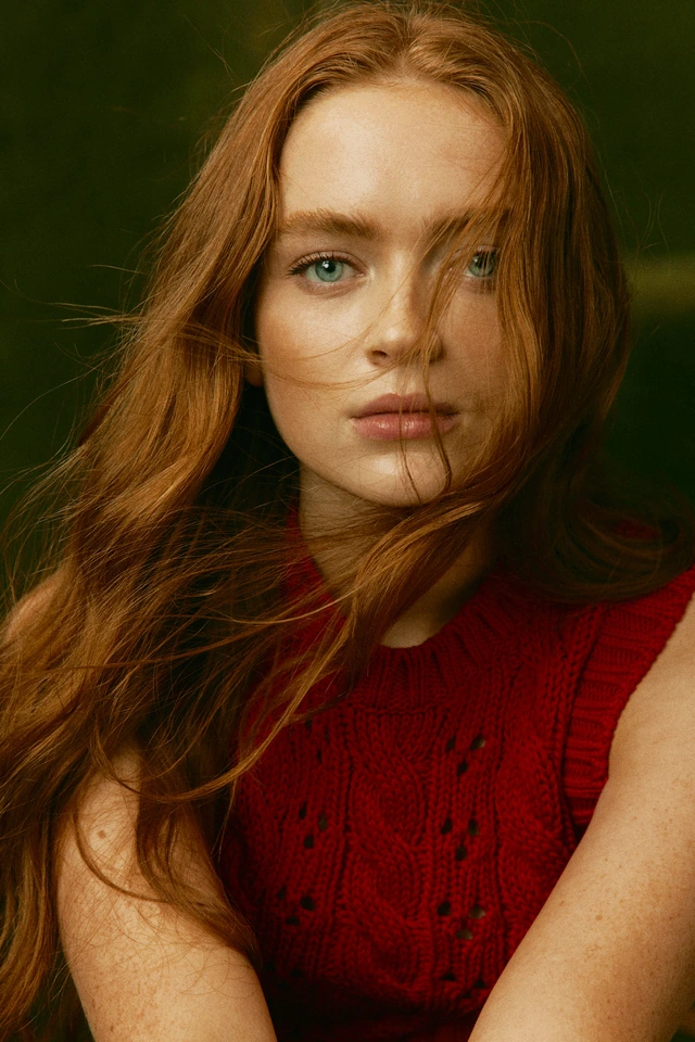 Actress Sadie Sink of Stranger Things, hair windswept across her face, red cable-knit vest, photographed by Austin Hargrave