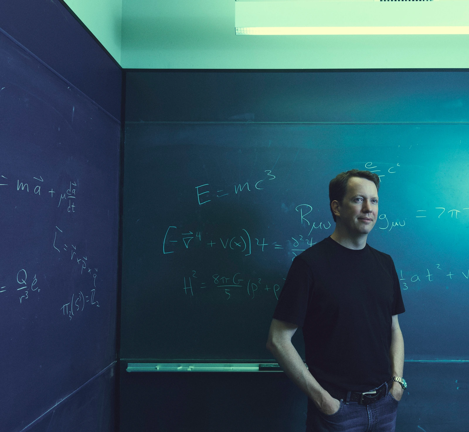 Theoretical physicist Sean Carroll, Mindscape host, relaxed before chalk equations on a teal-lit blackboard, by Austin.