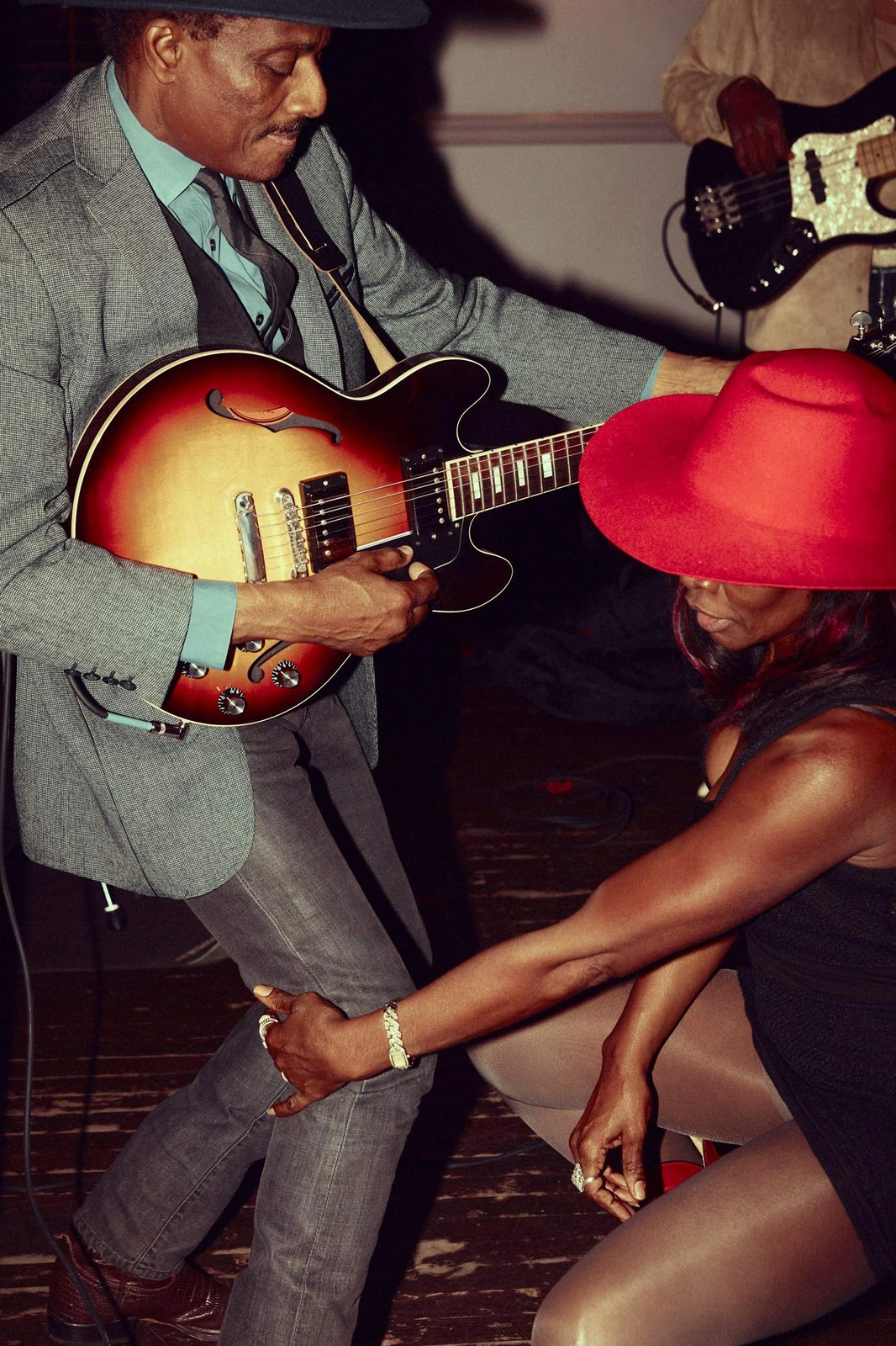 South Side Music — guitarist in grey blazer and teal shirt leans into a sunburst hollow-body as a dancer in a red hat kneels.