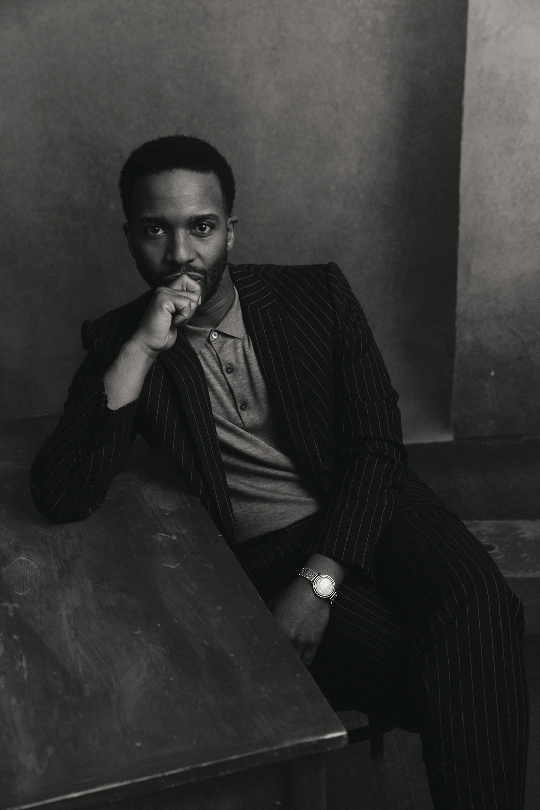 Playwright Tarell Alvin McCraney, Academy Award winner for Moonlight, in pinstripe suit, hand to chin, brooding B&W portrait.