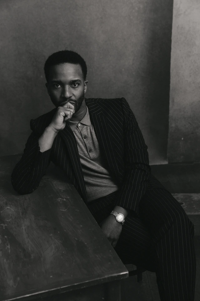 Playwright Tarell Alvin McCraney, Academy Award winner for Moonlight, in pinstripe suit, hand to chin, brooding B&W portrait.