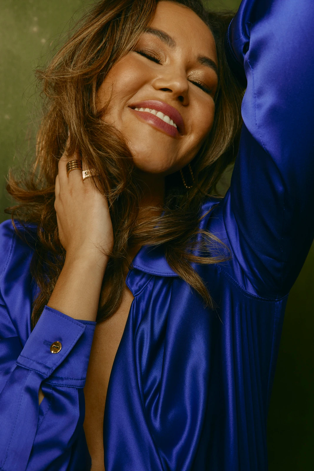 Actor Solea Pfeiffer eyes closed, radiant smile, in a cobalt satin shirt, gold rings, warm light against olive — TIFF 2022.