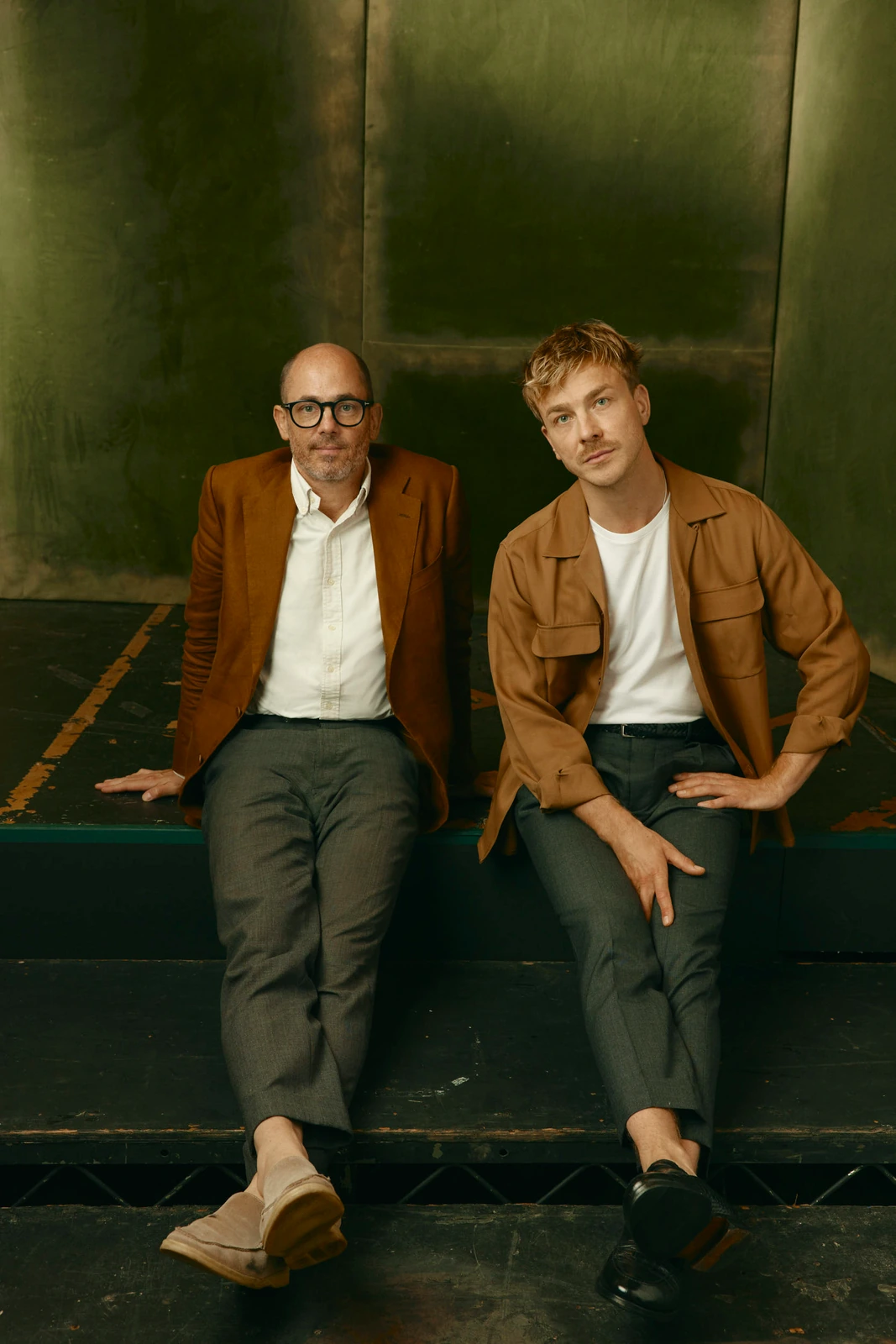 Director Edward Berger and actor Albrecht Schuch seated on a stage riser, both in warm caramel tones against a dark.