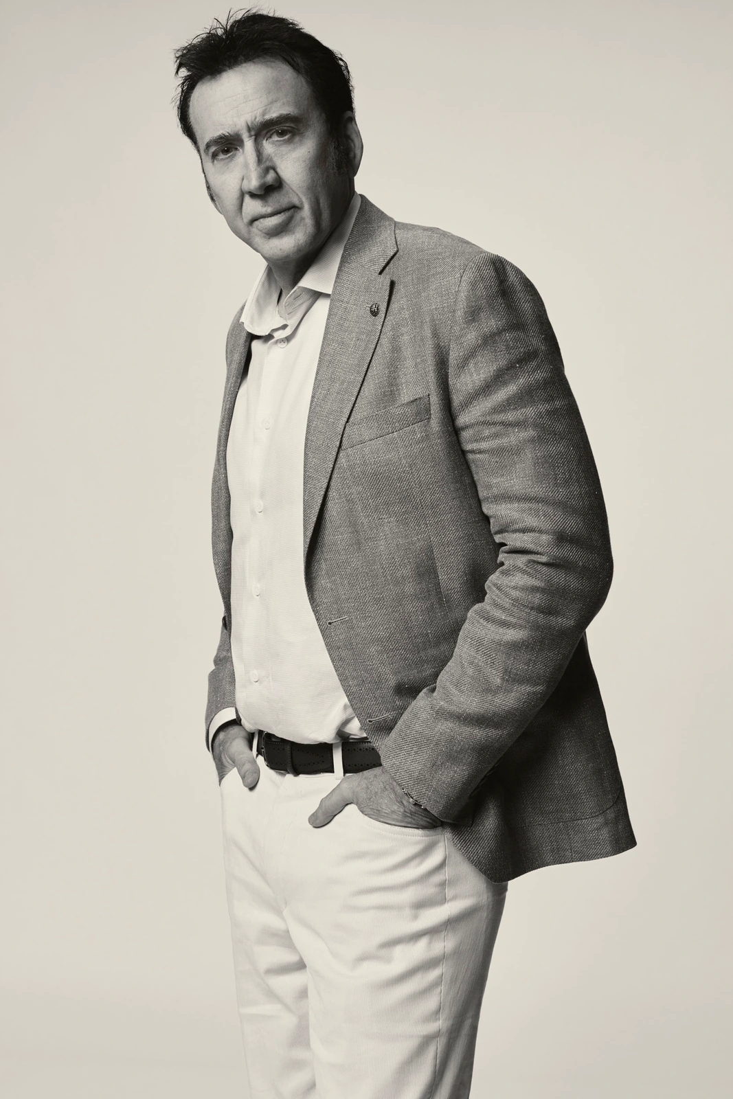 Actor Nicolas Cage, hand in pocket, in a linen blazer and white trousers, sharp gaze over shoulder, black-and-white TIFF.