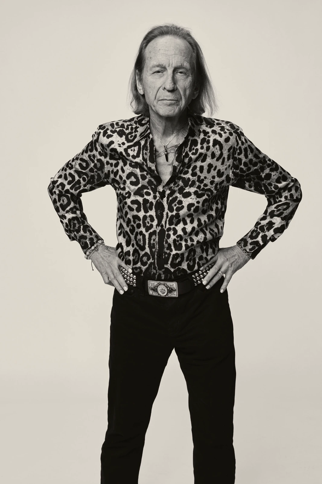 Actor Paul Raci at TIFF 2022, hands on hips in a leopard-print shirt and studded belt, steady gaze against pale gray.