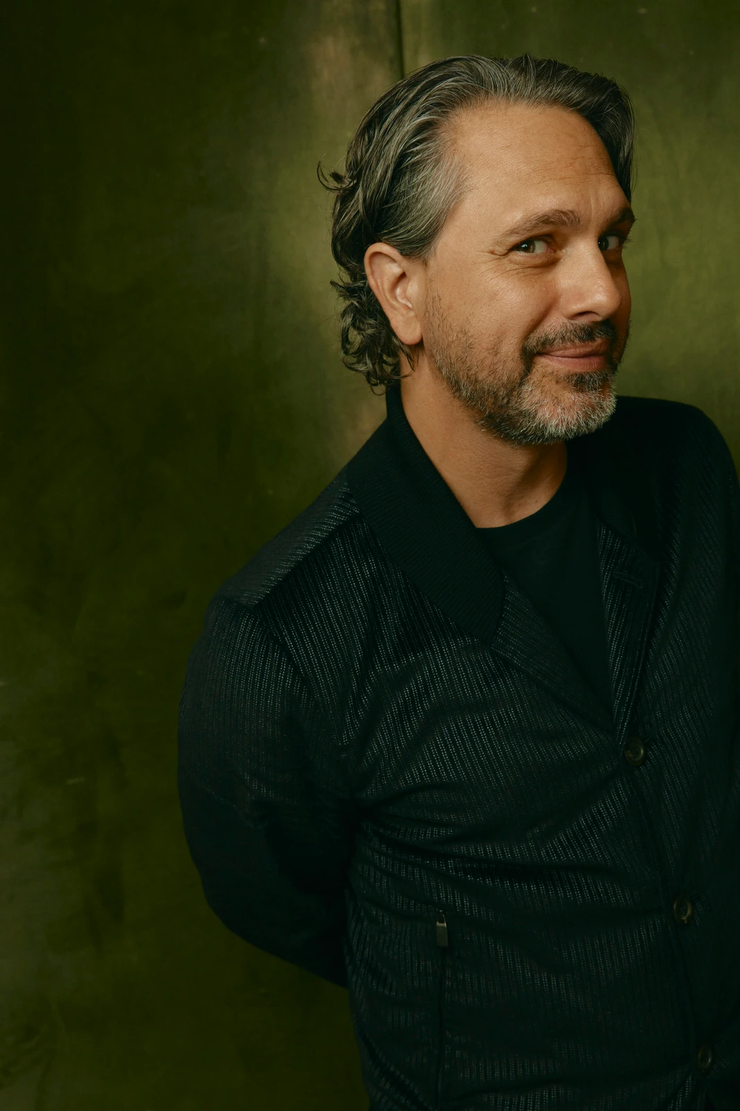 Actor Thomas Sadoski at TIFF 2022, half-smiling gaze off-frame in a dark knit jacket, leaning against a deep olive wall.