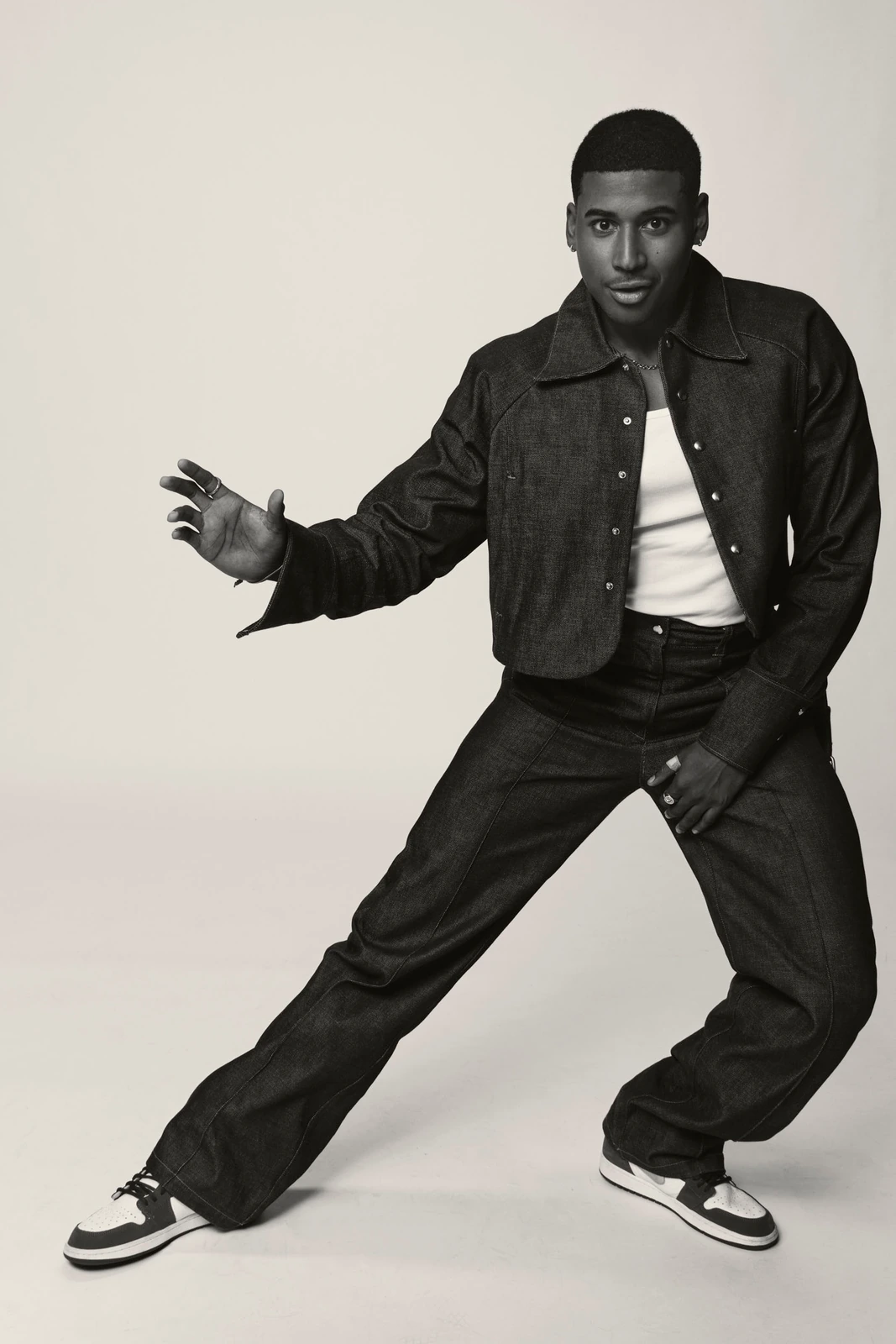 Actor Michael Cooper Jr. in a wide-stance dynamic pose, dark denim set over a white tee and Air Jordan 1s, black and white.