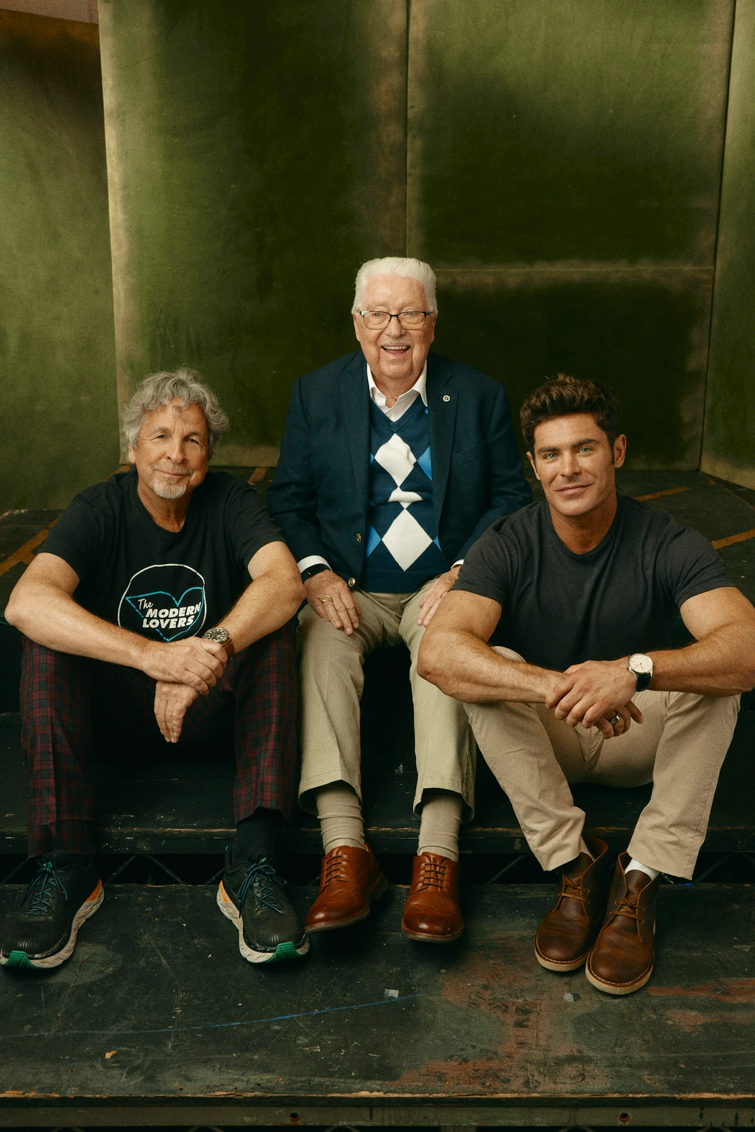 Director Peter Farrelly, John 'Chickie' Donohue, and actor Zac Efron seated together at TIFF 2022, warm brass tones behind.