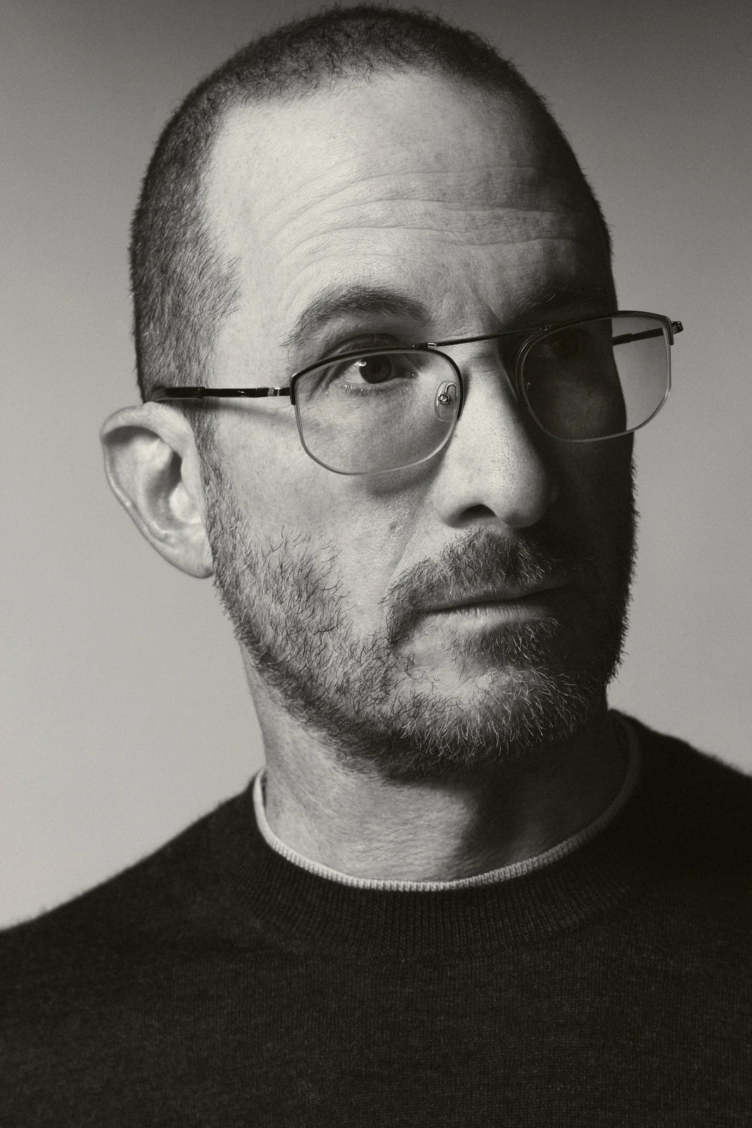 Director Darren Aronofsky, wire-frame glasses and cropped stubble, steady gaze in a stark B&W close portrait, TIFF 2022.