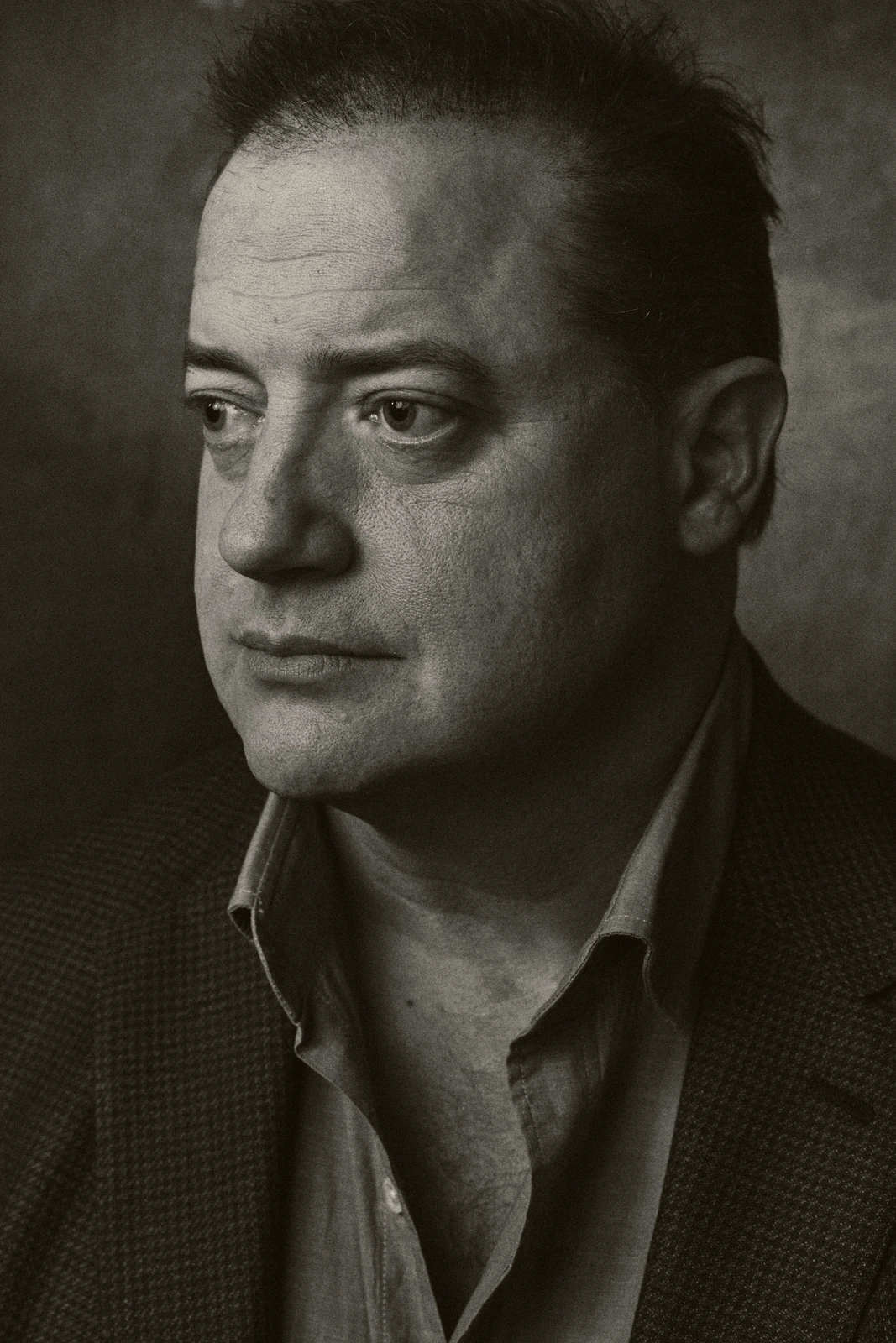 Actor Brendan Fraser in a moody black-and-white portrait, open collar and dark blazer, gaze averted, at TIFF 2022.