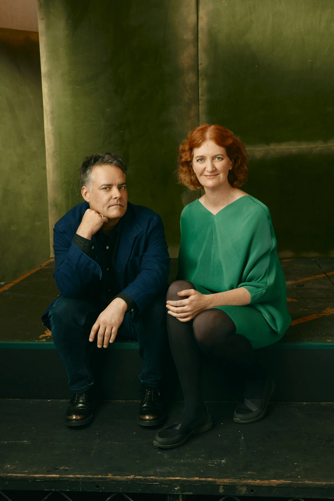 Director Sebastián Lelio and author Emma Donoghue seated on dark steps against a patinated green wall, TIFF 2022.