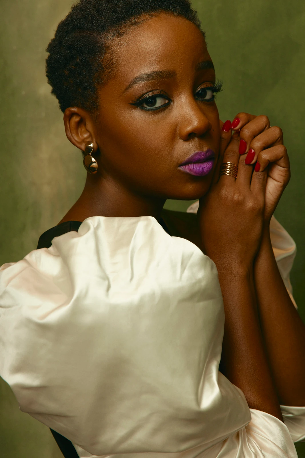 Actor Thuso Mbedu, violet lips and red nails against a cream ruffled gown, gaze sidelong in warm olive light at TIFF 2022.