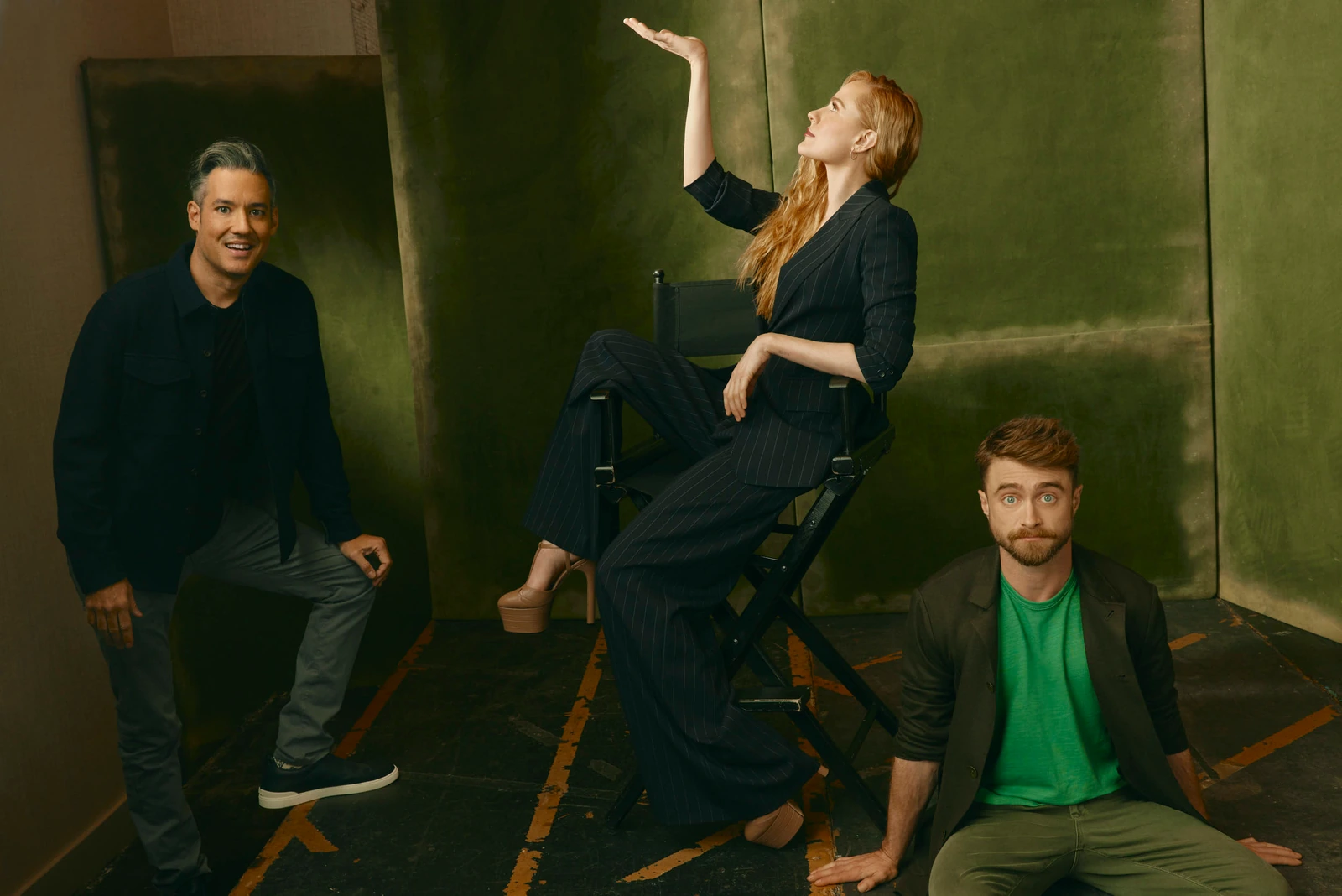 Director Eric Appel, actor Evan Rachel Wood, and Daniel Radcliffe in a moody green studio at TIFF 2022, Wood reaching.