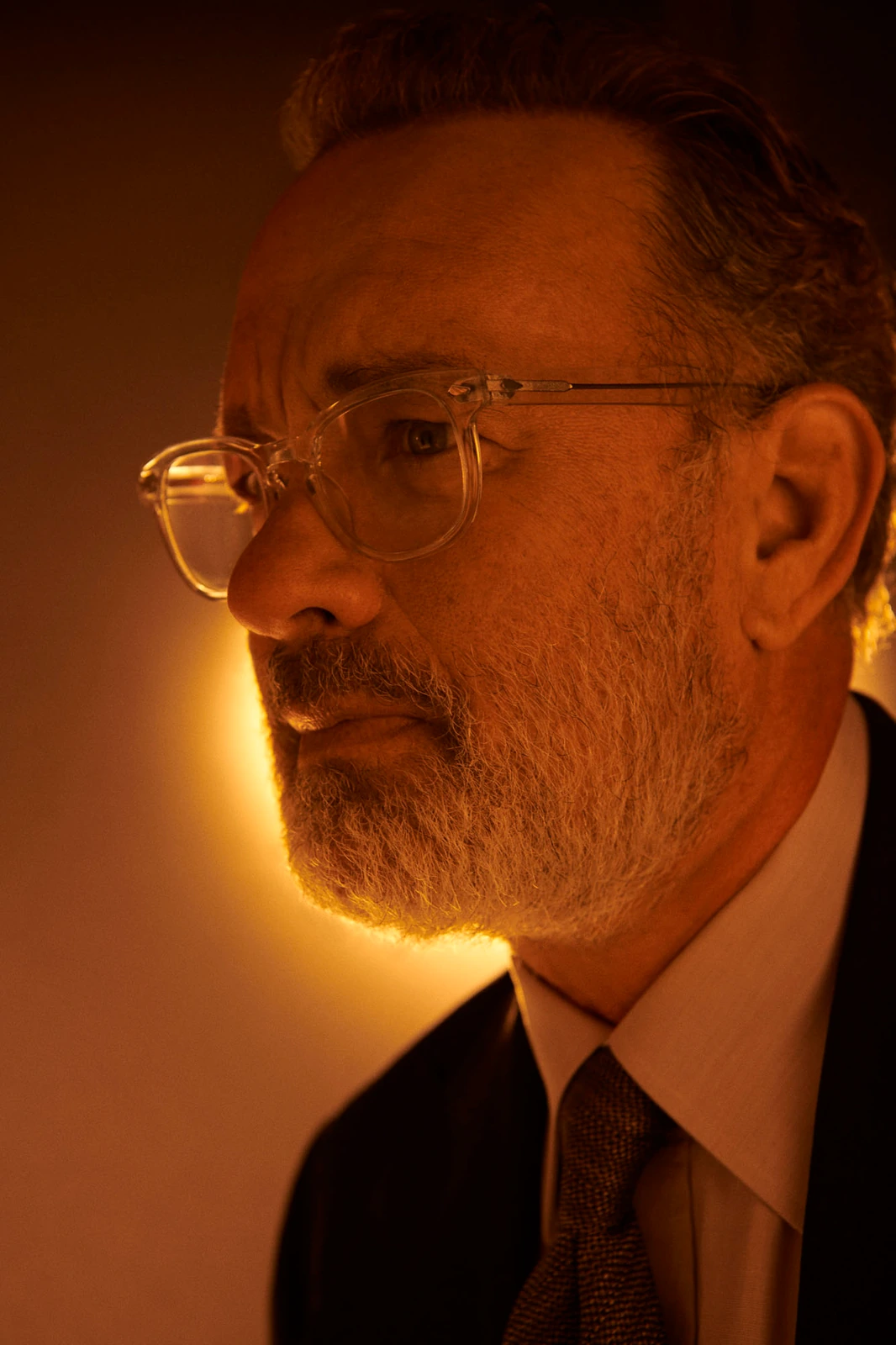 Actor Tom Hanks in clear-frame glasses and dark suit, gaze drifting left in deep amber light at TIFF, photographed by Austin.